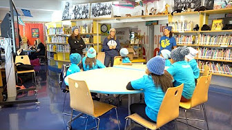students in blue hats seated in school library